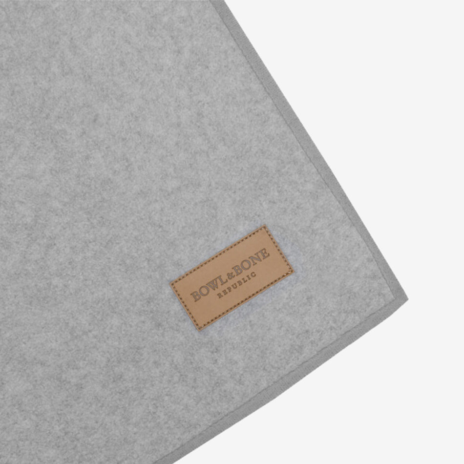 A close-up of a gray fabric mat with a brown leather label that reads "BOWL&BONE REPUBLIC."