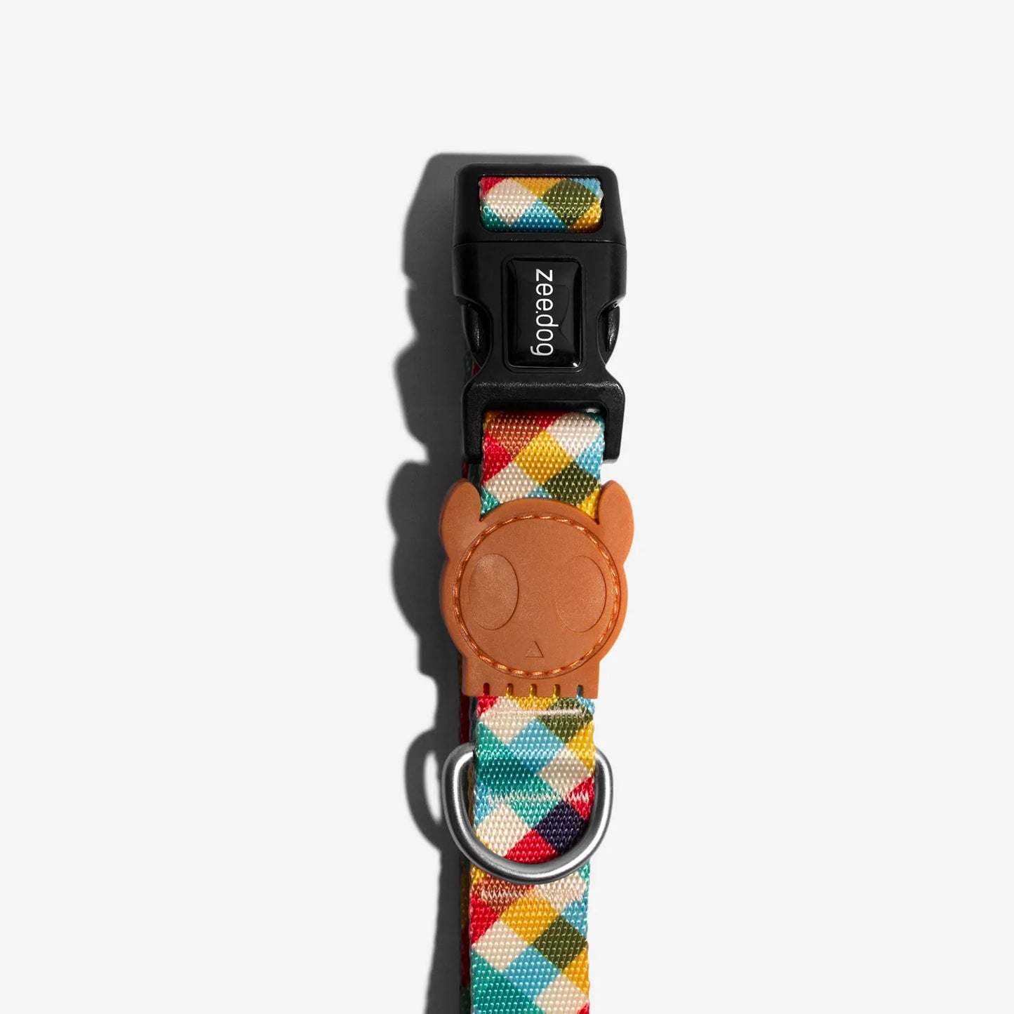 Colourful dog collar with a tan leather tag featuring a cartoon face, showcasing a snap buckle and metal D-ring for leash attachment.