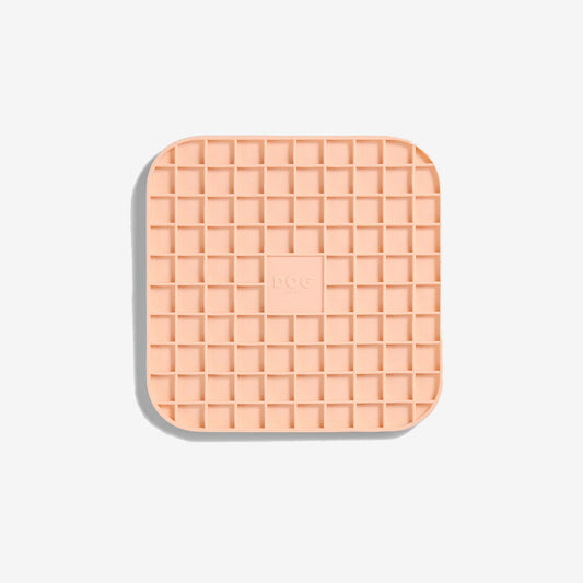 A blush coloured square lickimat with rounded edges and gridded squared inner pockets 