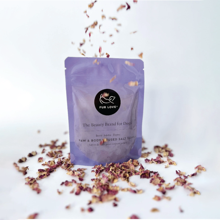 A lilac pouch filled with paw and body infused salts, surrounded by dried petals.