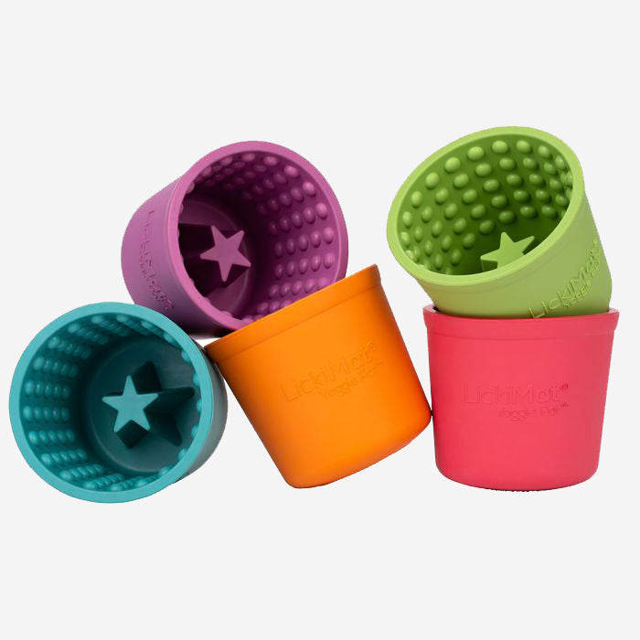 Five textured Licki Mat dog feeding pots, in orange, turquoise, purple, red and lime green with raised bumps inside, on a plain background.