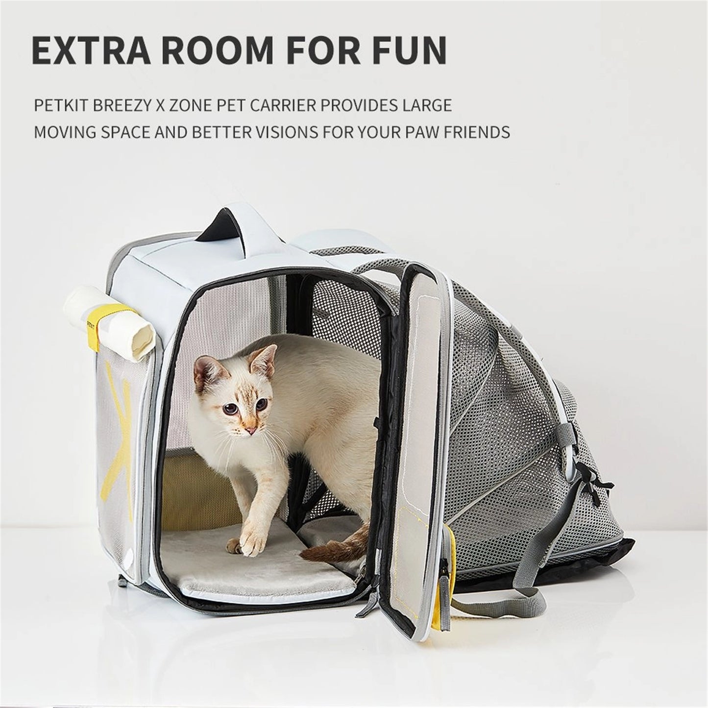 A white cat inside a grey pet backpack by PetKit with extra tent space, featuring a yellow storage compartment on the side.