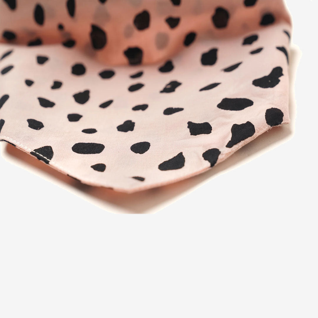 Close up fabric of a 100% cotton dog bandana with black leopard spots on pale pink