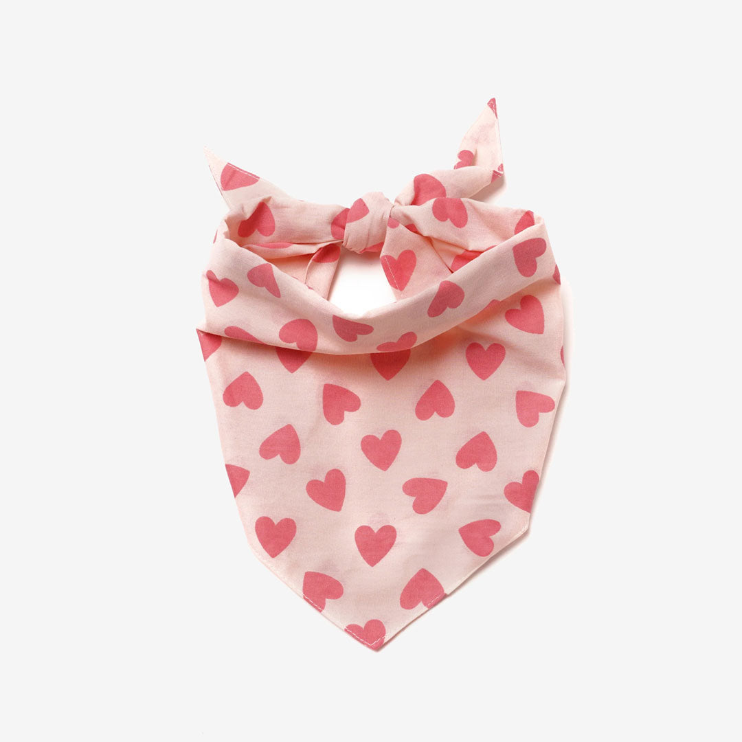 Close up fabric of a 100% cotton dog bandana patterned with rose coloured pink heart on pale pink