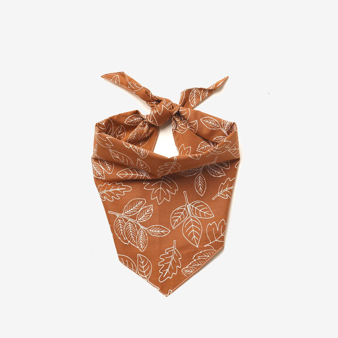 A100% cotton dog bandana patterned with white outlined leaves on a rust base 