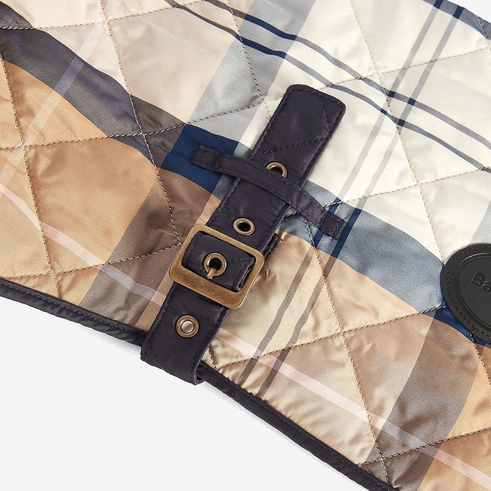 Close-up of a quilted fabric featuring a plaid pattern in warm tones, secured with a leather strap and buckle.