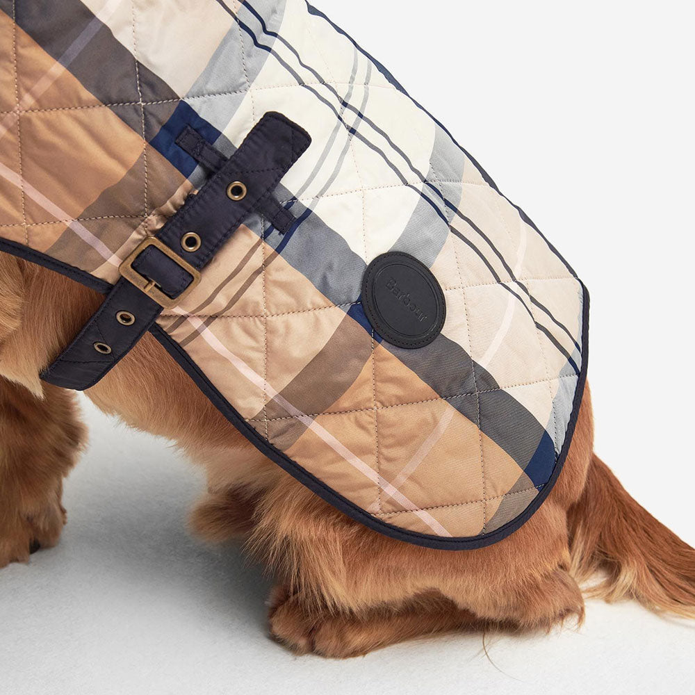A close-up of a dog wearing a stylish, quilted plaid coat with a buckle and logo patch, showcasing its warm and fashionable design.