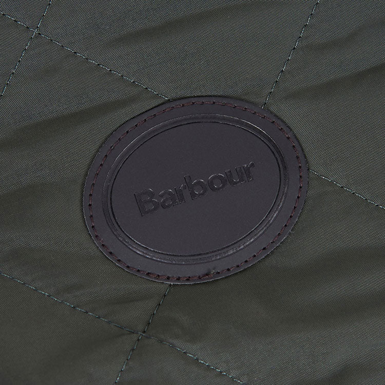 Close-up of a dark green quilted fabric featuring an embossed black leather Barbour logo patch.