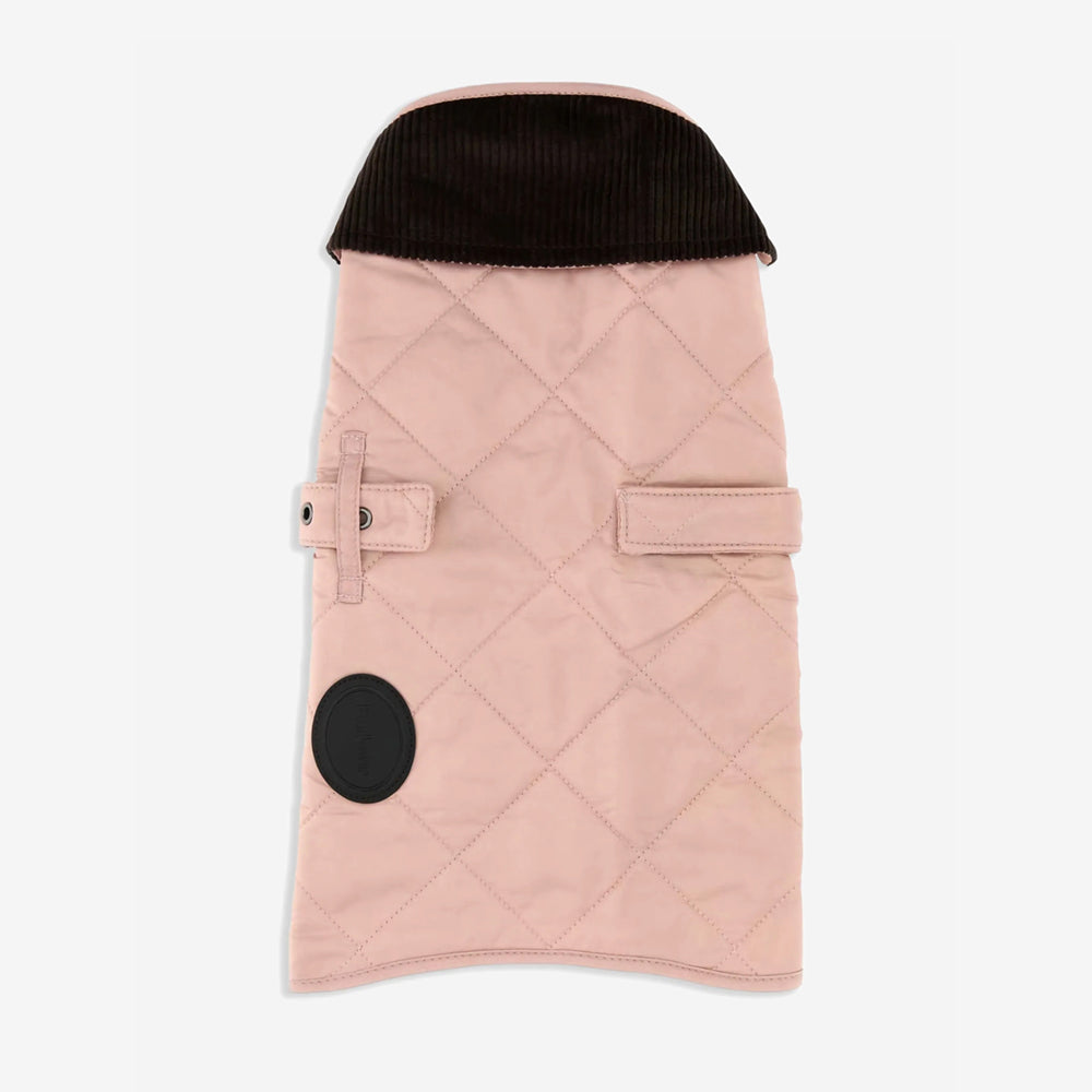 A light pink quilted dog coat with a dark corduroy collar and two adjustable straps, featuring a round brand patch.