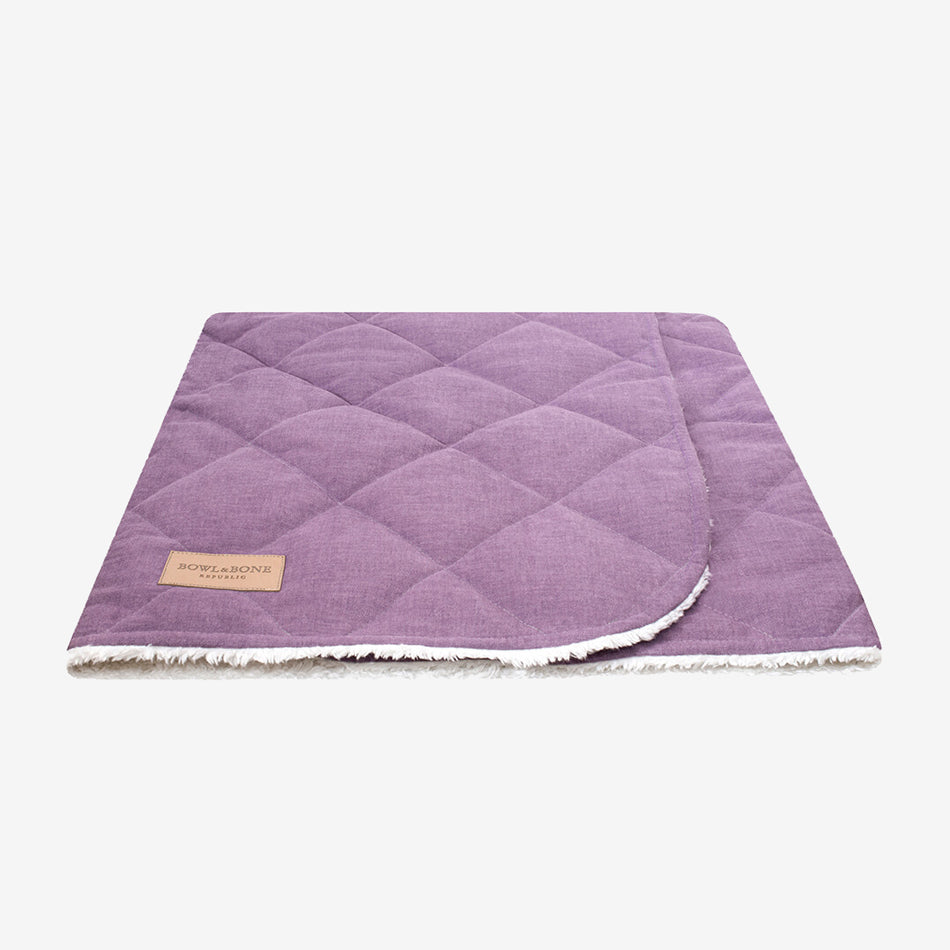 A closed purple dog blanket/sleeping bag quilted fully and fully lined with a cream fluffy inner