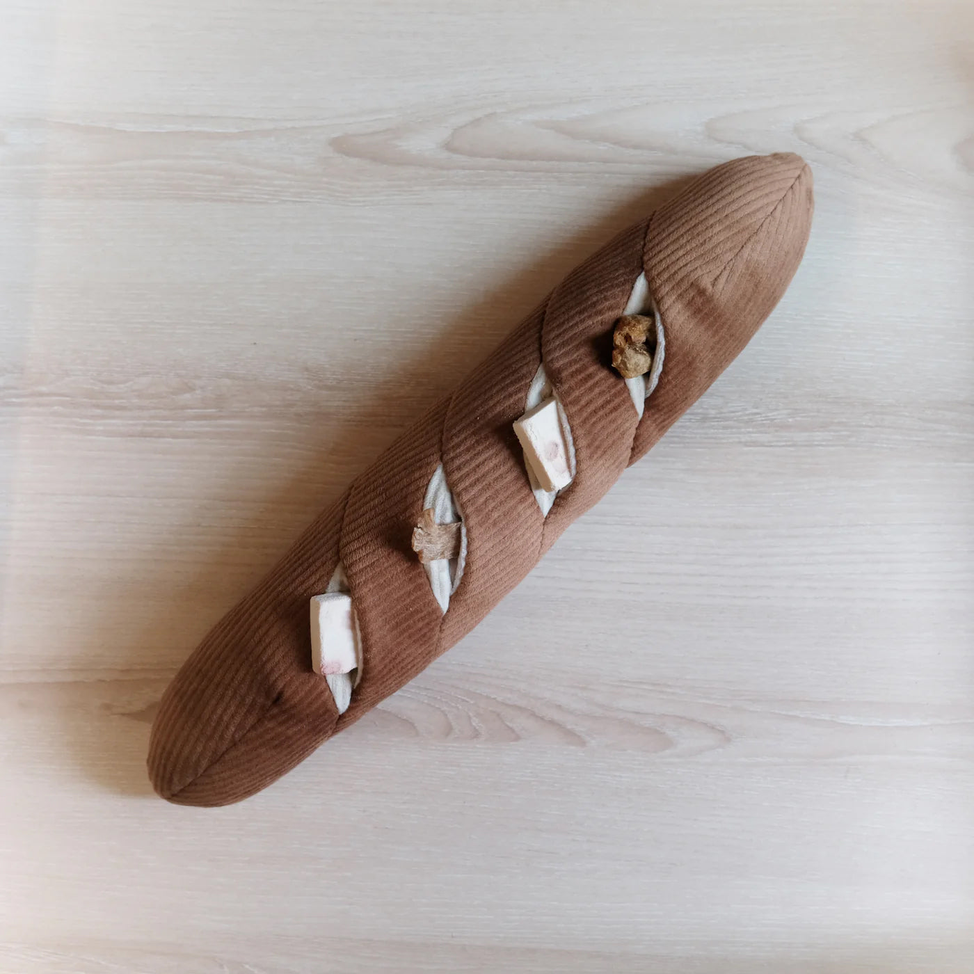 A large brown plush baguette dog toy. The baguette has four snuffle pockets with dog treats inside.