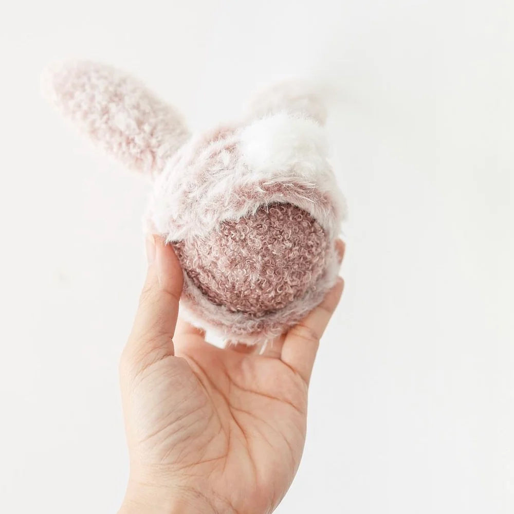 Hand holding a plush pink bunny ball dog toy.