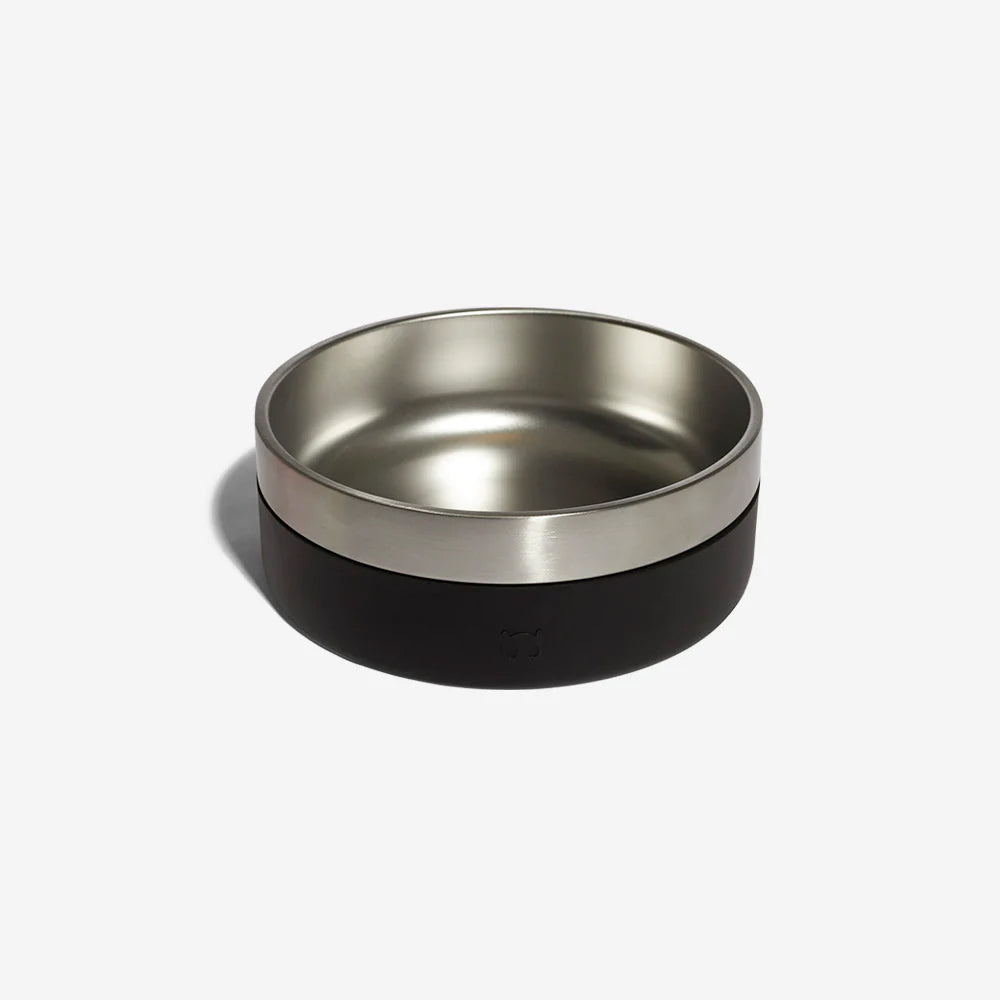 A stainless steel dog bowl with a black rubber exterior by Zee Dog with kibble in resting against a plain white background.