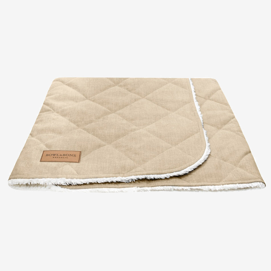 A closed beige dog blanket/sleeping bag quilted fully and fully lined with a cream fluffy inner